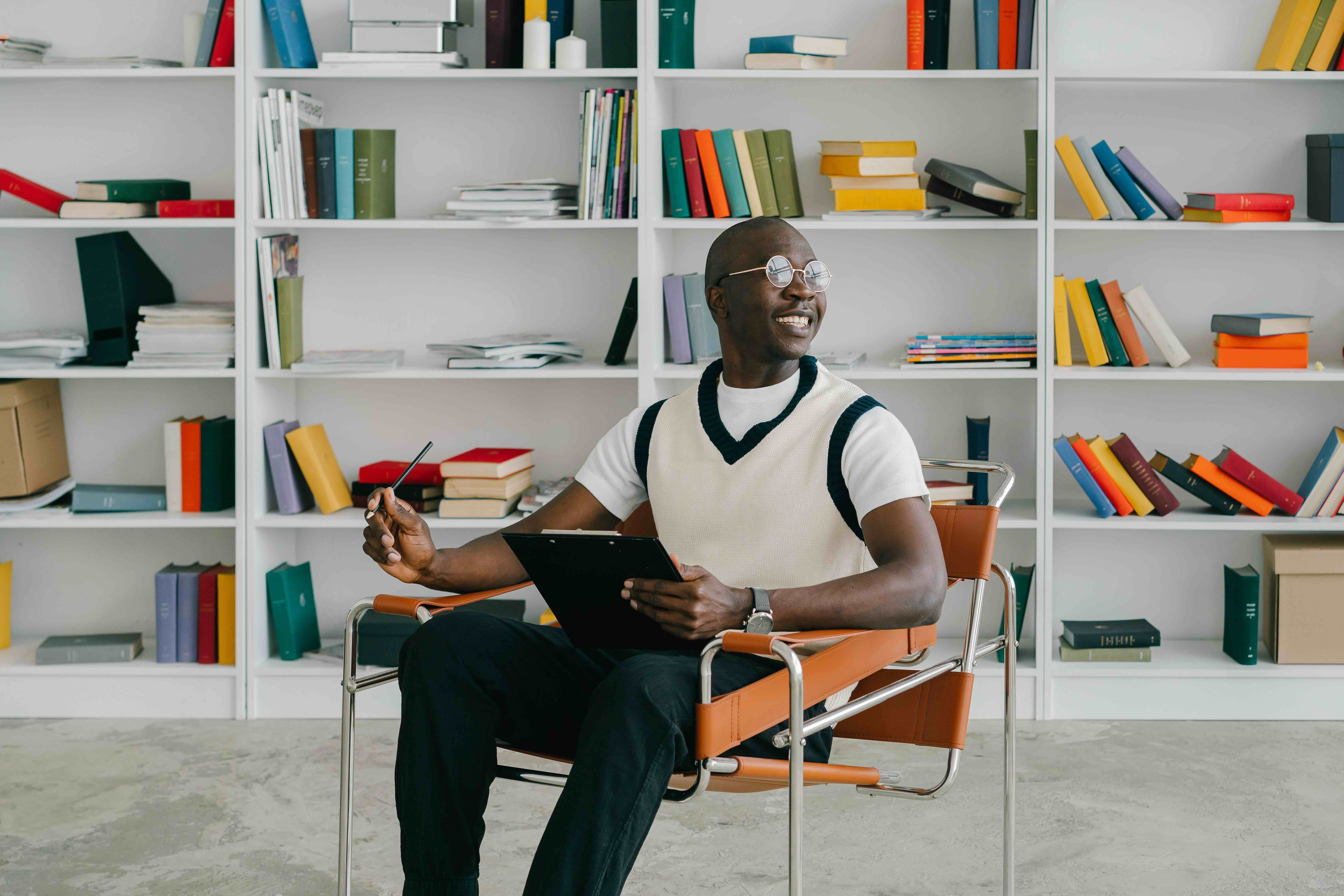 One man sitting on a chair with a notepad. There is a bookshelf behind him.